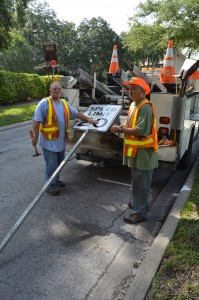 Danny Williams and Gary LaFrance, both traffic engineers with the city Public Works Department, get ready to install a 20 mph speed limit sign along River Road July 28.