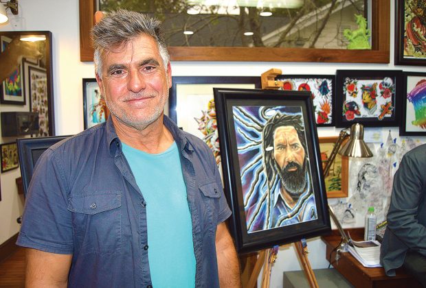 Author Jim Alabiso stands with a portrait of one of the characters from his work, “All the Angels Come” at Sunday Tattoo