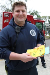 EMT firefighter Colton Philips, from Ladder 10, holds “thank-you” cards created by West Riverside Elementary School students.
