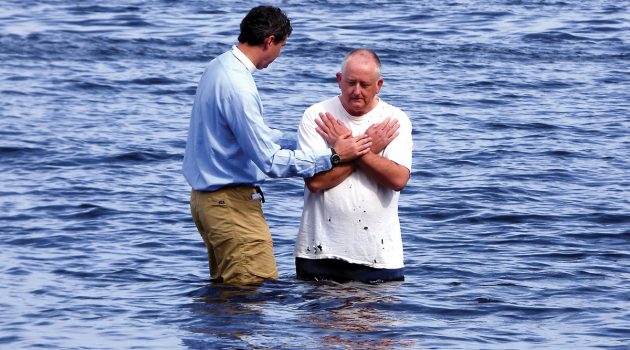 Gathering at the river, local pastor baptizes by immersion