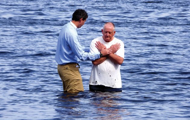 Gathering at the river, local pastor baptizes by immersion