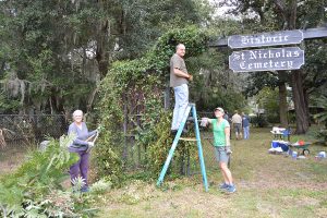 Ginger and Bunker McClendon trim the bushes near the Historic St. Nicholas Cemetery sign while Beth Pavlicberry looks on during a clean-up day that was part of neighbor Will Weinbecker’s Eagle Scout project Nov. 4.