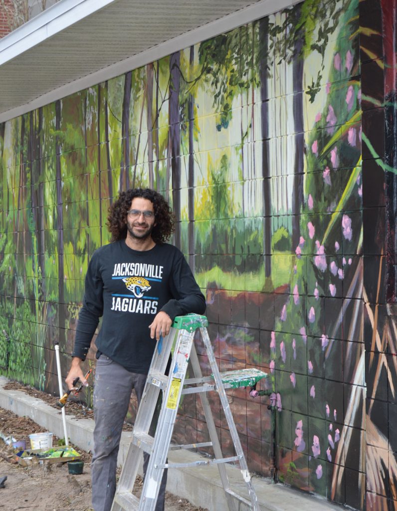 Springfield artist David Nackashi standing alongside the mural he is painting on the former “Little Gray House” on the Southbank Riverwalk.
