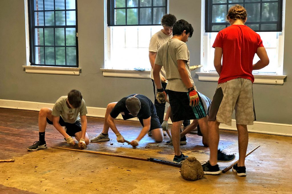 Boy Scout Troop 2 members hand-scrape glue from 80-year-old wood flooring.