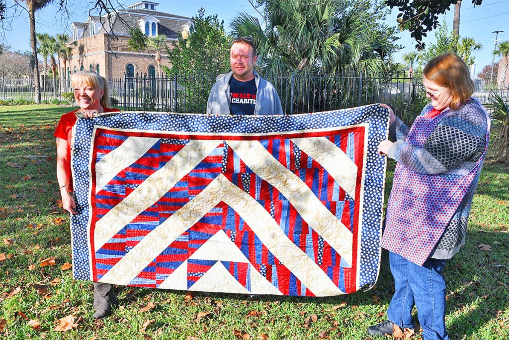 Christmas Breakfast in the Park founder Cynthia Saben, with volunteer Elizabeth Haugen and veteran David McGuffin, for whom the quilt was given. The quilt, named The Quilt of Valor, was created and donated by Haugen's friend, quilter Lorraine Happy.