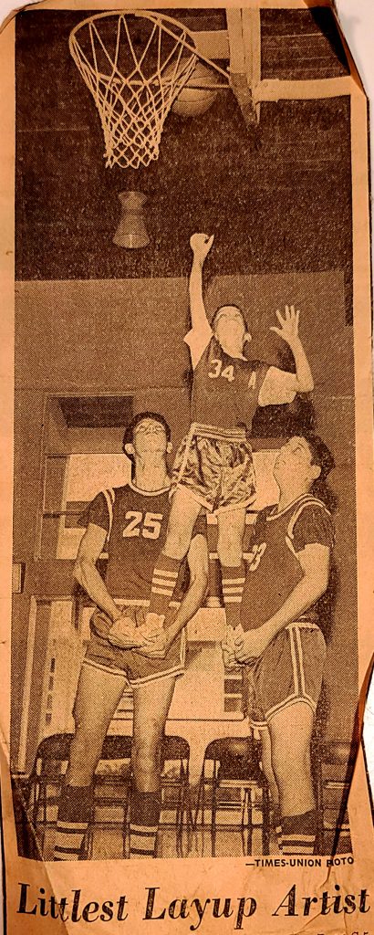 A newspaper clipping with Ken Juro on the right-hand side holding up the water boy for the Assumption basketball team.