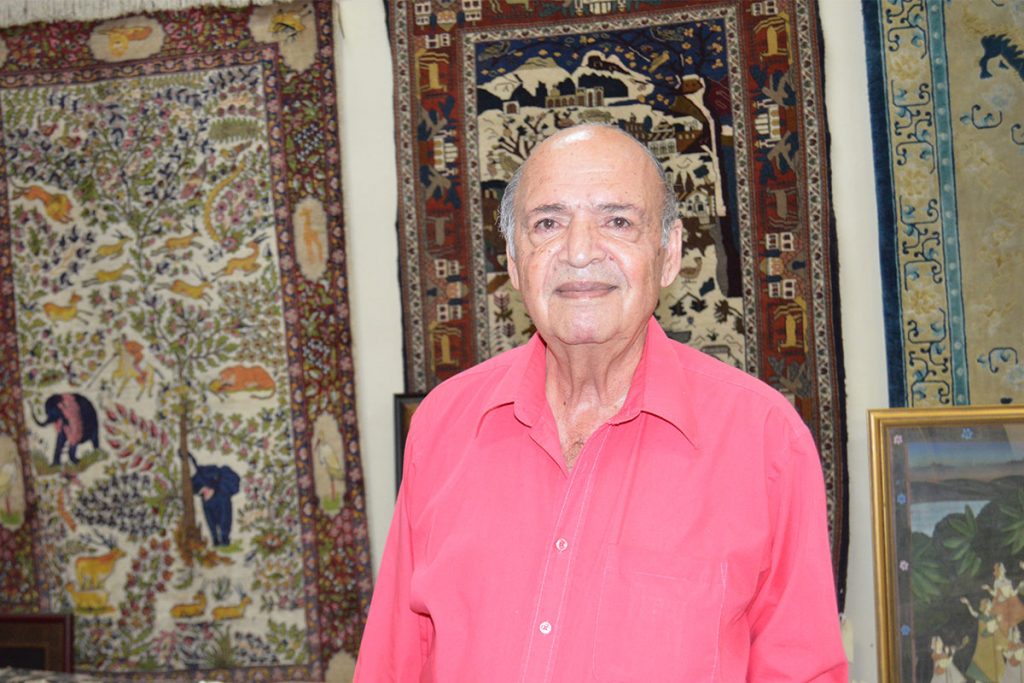 Hooshang Harvesf with rugs hanging behind him
