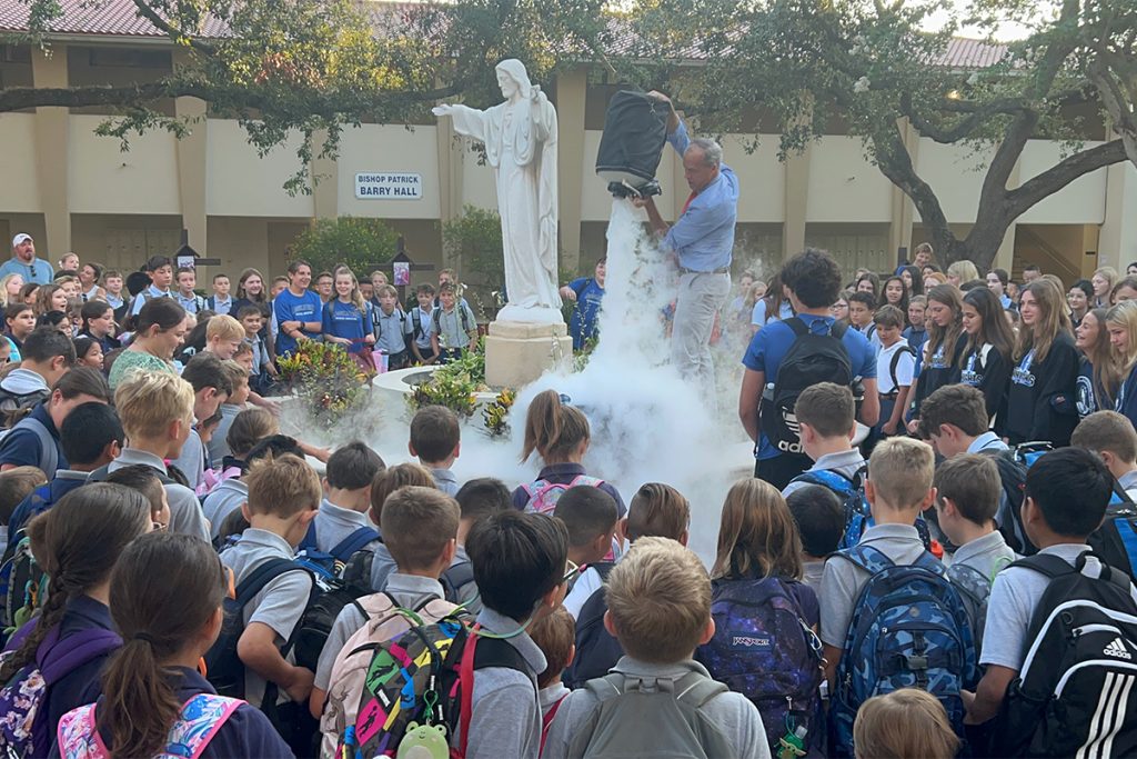 large crowd of kids around statue with man pouring bucket onto statue pedestal