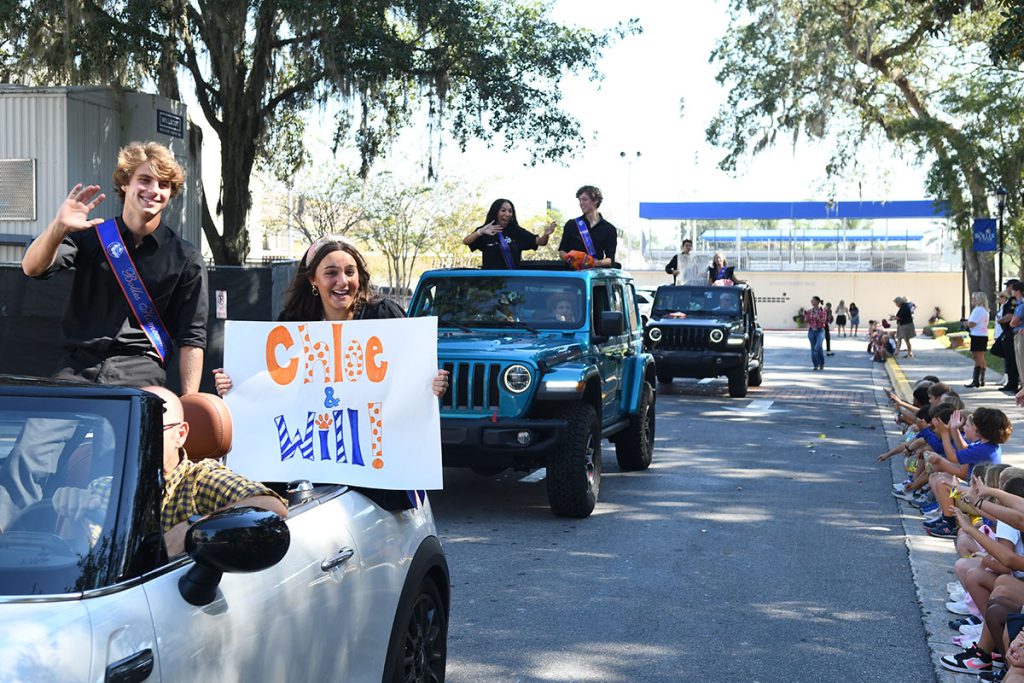 smiling students riding in vehicles in parade