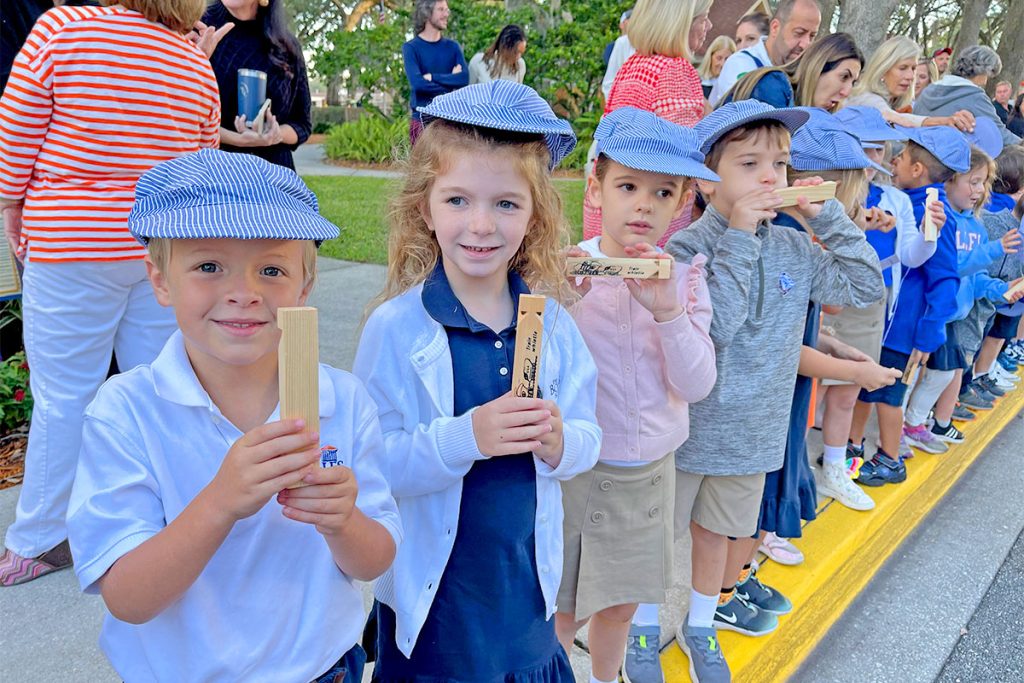 kids smiling with wooden train whistles and wearing train caps