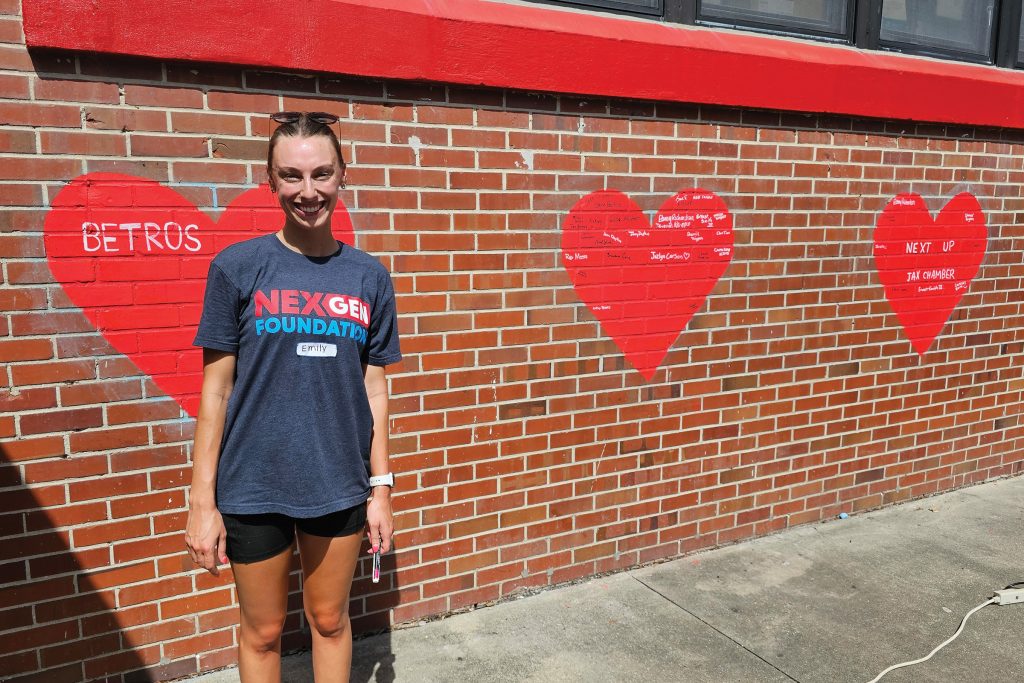 Emily Urubu in front of a row of painted hearts bearing the names of the volunteers from the 2024 San Jose Elementary Work Day.