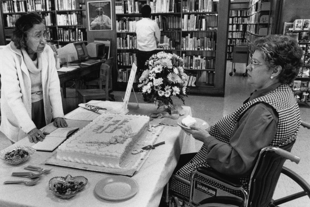 Two women visit over a sheet cake celebrating the 40th anniversary of the San Marco Branch Library in 1990.