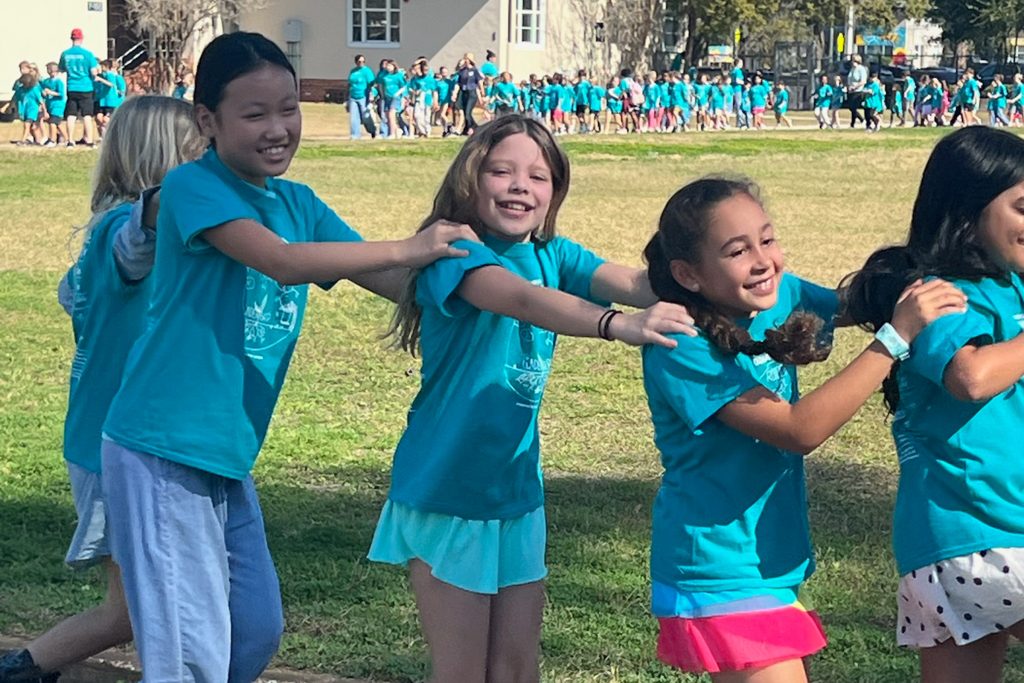 students walking and smiling in a line with hands on each others' shoulders