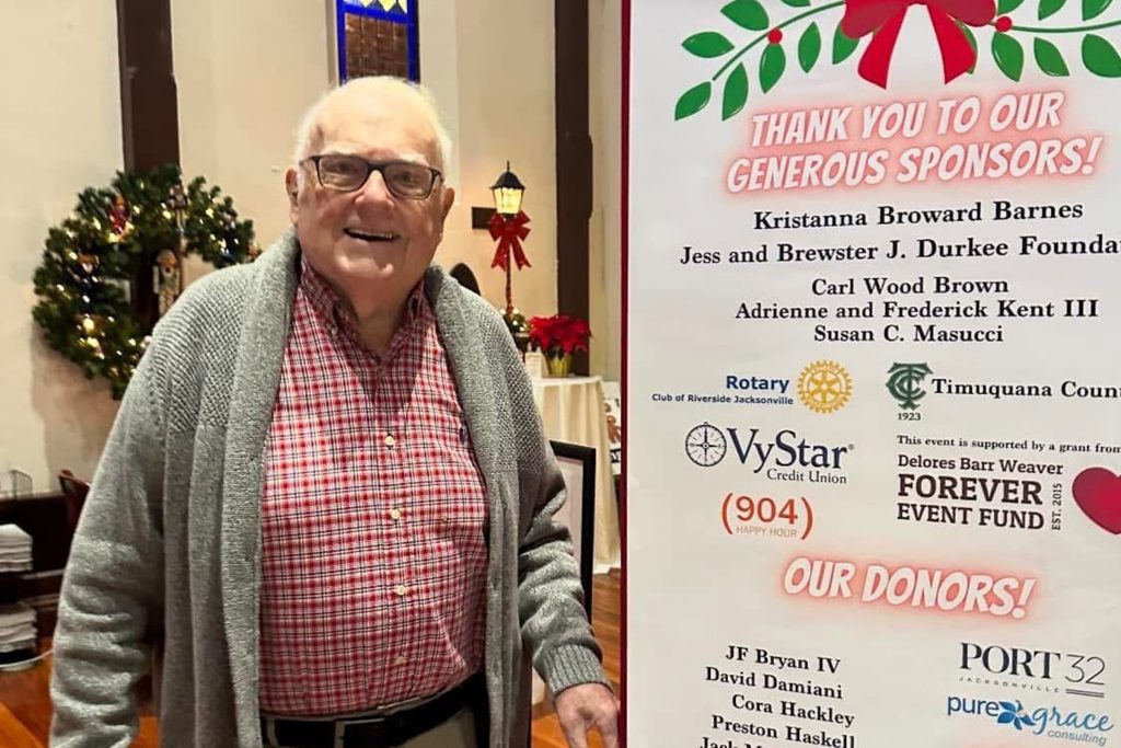 Carl Wood Brown “Skip” standing in church next to "Thank You to Our Generous Sponsors" sign, with his name listed among sponsors