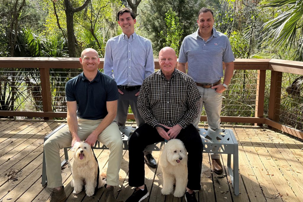 Michael McGowan standing with Deno Hicks and father-and-son duo Chase and Michael Balanky pose on the Emerald Trail with the TrailView property in the background. With them are pups Barkley and Sailor.