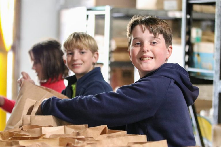 2 boys smiling and placing items in paper bags