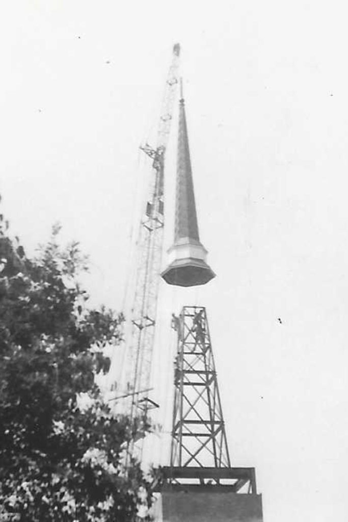 black and white photo of steeple being placed on building