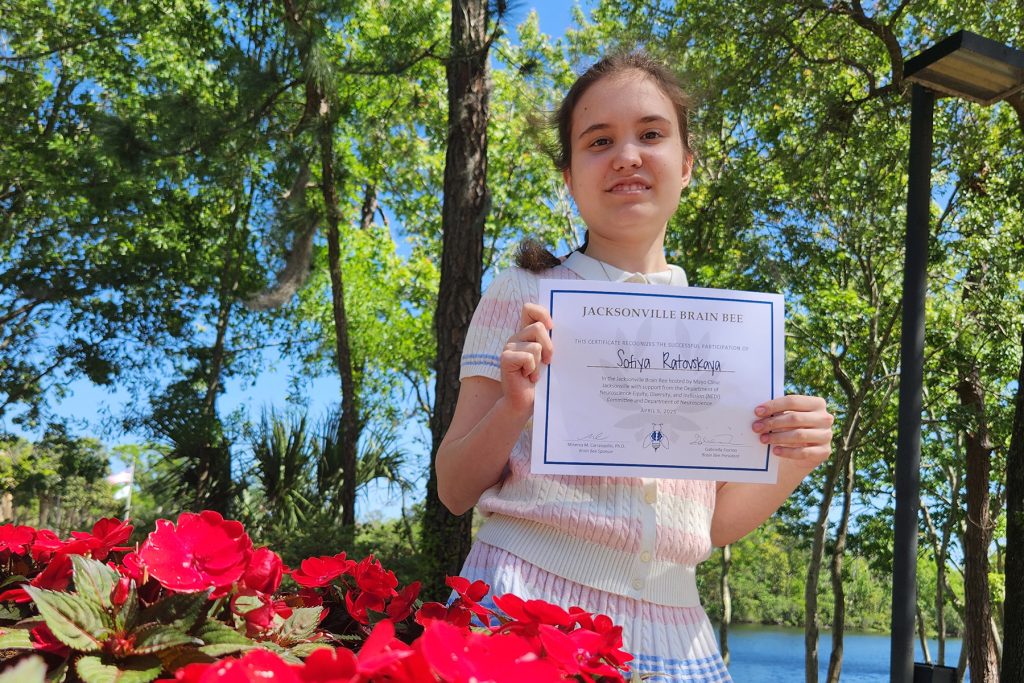Sofiya Radlovskaya smiling and holding up Brain Bee certificate