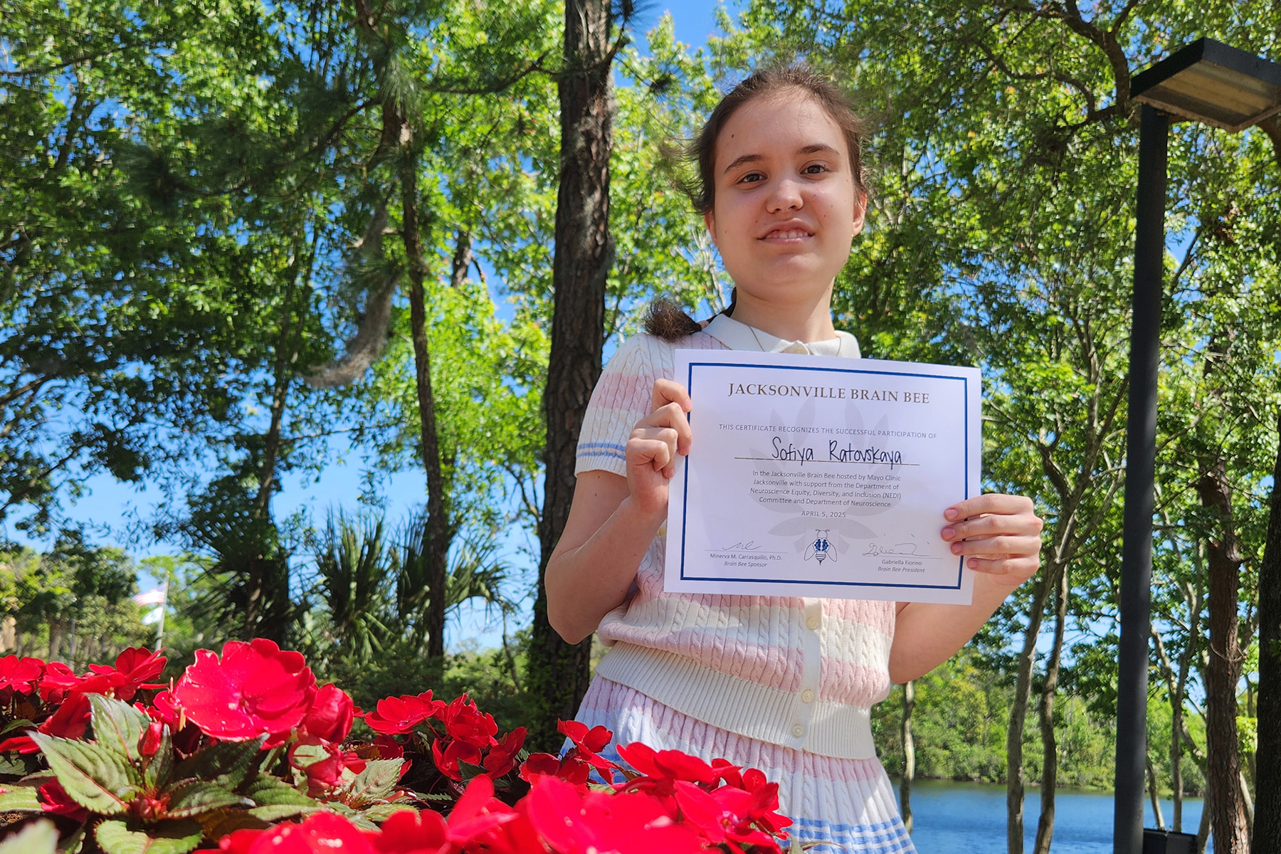 Sofiya Radlovskaya smiling and holding up Brain Bee certificate