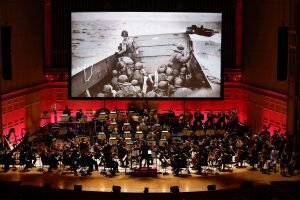 orchestra playing music with WWII image on screen