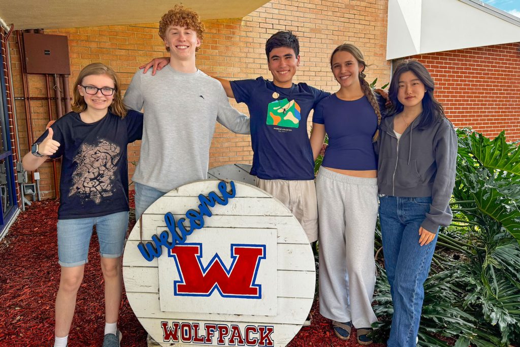 students smiling with wooden "Wolfpack" sign