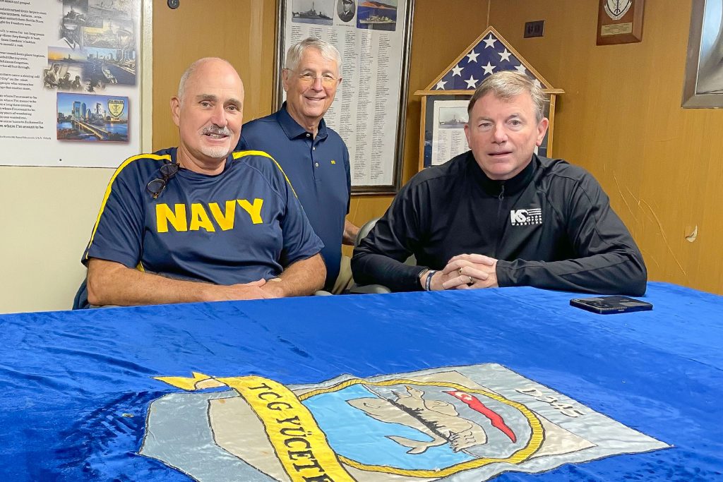 Ship Manager and Retired Navy Captain James F. Fossa with William Harrell and Dan Bean at the table in the USS Orleck’s wardroom, where the Turkish Navy embroidered cover is on display.