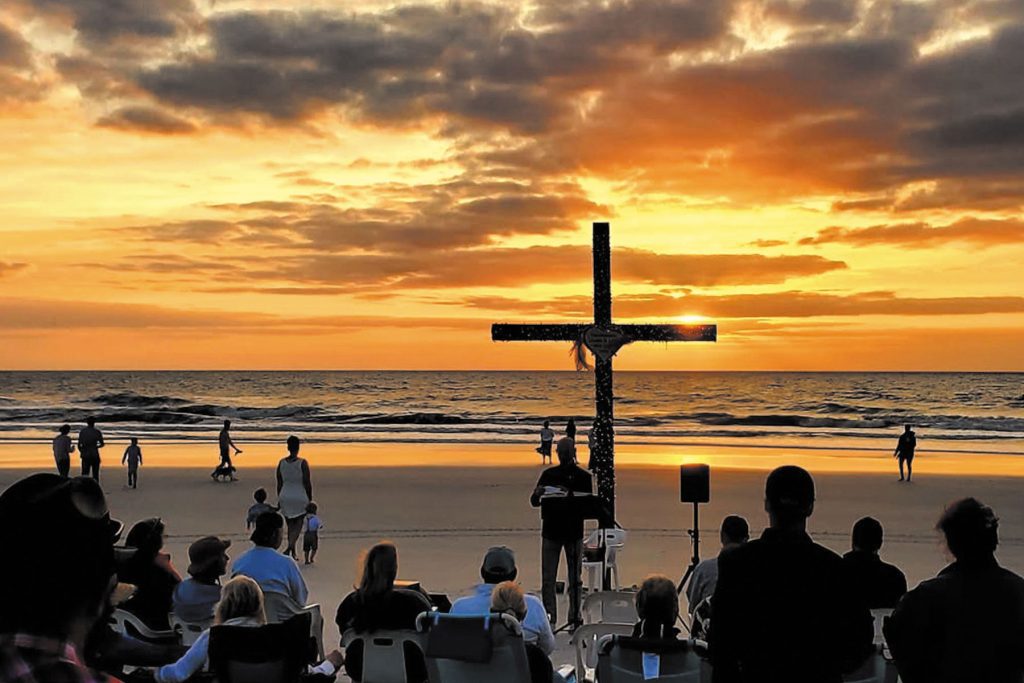 people at the beach, with a cross planted in the sand