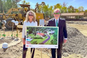Daniel CEO Lesley Wells and Chairman of the Board of Trustees Judge Timothy Corrigan pose beside a rendering of the new cottage at the March 11 groundbreaking ceremony.